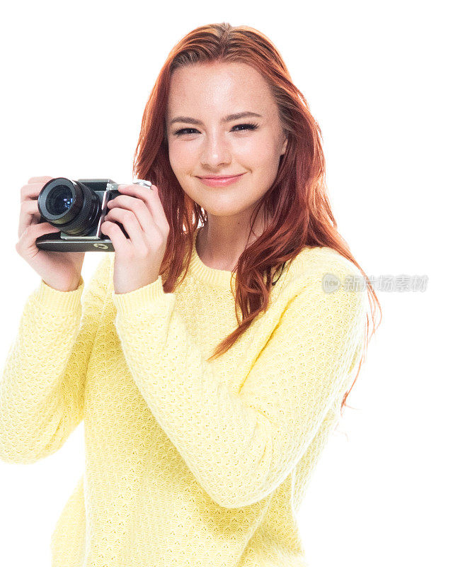 腰部以上的18-19岁美丽的红发白人年轻女性十几岁的女孩/摄影师/摄影/游客在白色的背景穿着牛仔裤/开襟毛衣谁是微笑/快乐/愉快谁是出汗/摄影